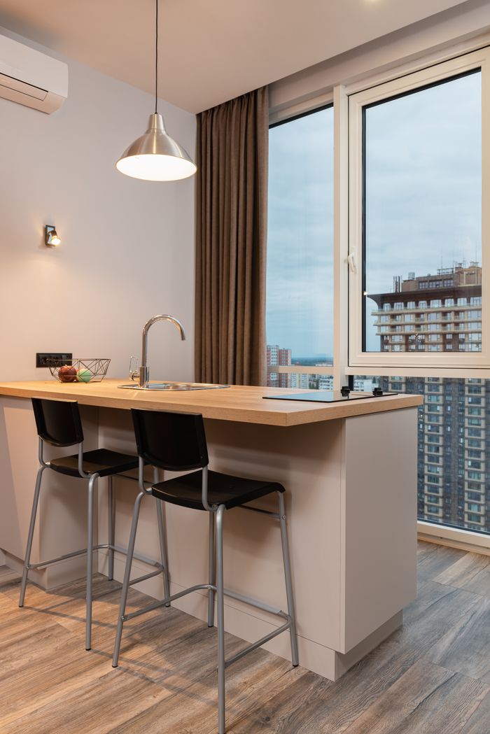 Interior of modern small kitchen with bar stools and table with inbuilt sink and cooktop near window